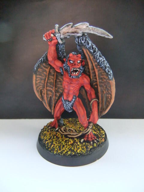 Photograph of a red winged demon miniature with raised sword on a round base.
