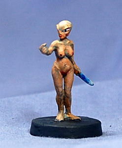 Miniature nude female figurine on a black base against a blue backdrop.