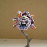Painted fantasy monster figurine with many eyes and a gaping mouth on a stand.