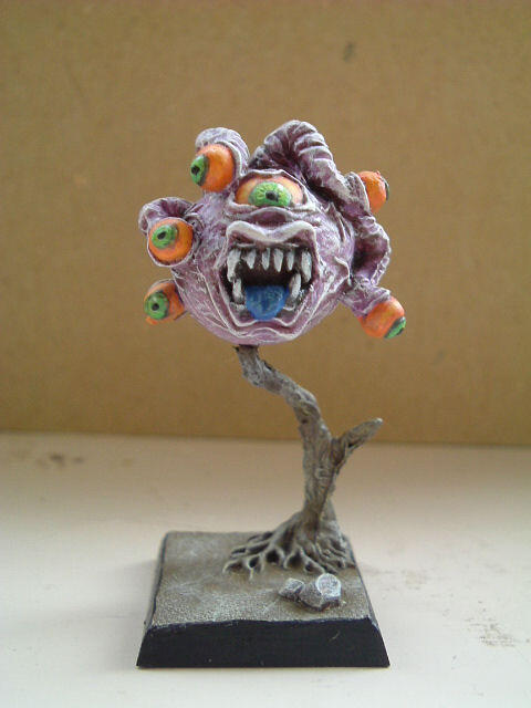 Painted fantasy monster figurine with many eyes and a gaping mouth on a stand.