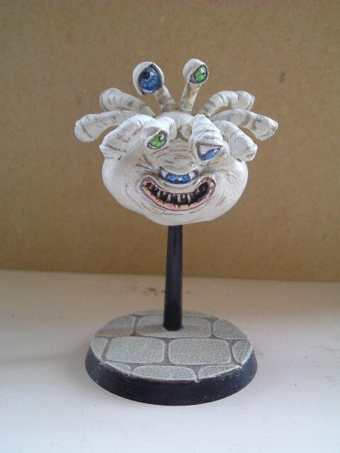 White clay face sculpture on a black stand, with blue eyes and a wide grin.