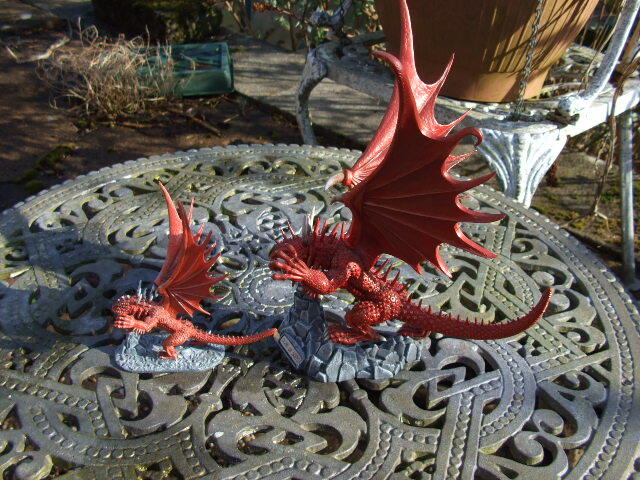 Two red dragon figurines on a patterned metal patio table outdoors.